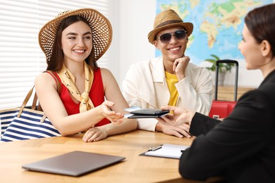 Photo of Happy couple planning vacation with travel agent at wooden table in office