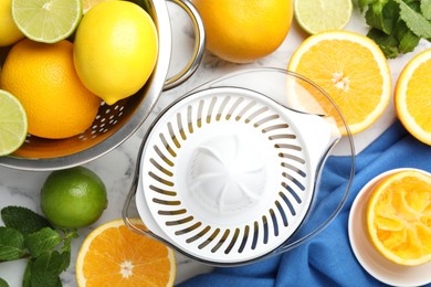 Photo of Plastic juicer and different citrus fruits on white marble table, flat lay