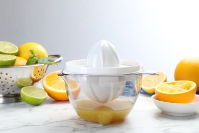 Photo of Plastic juicer and different citrus fruits on white marble table, closeup