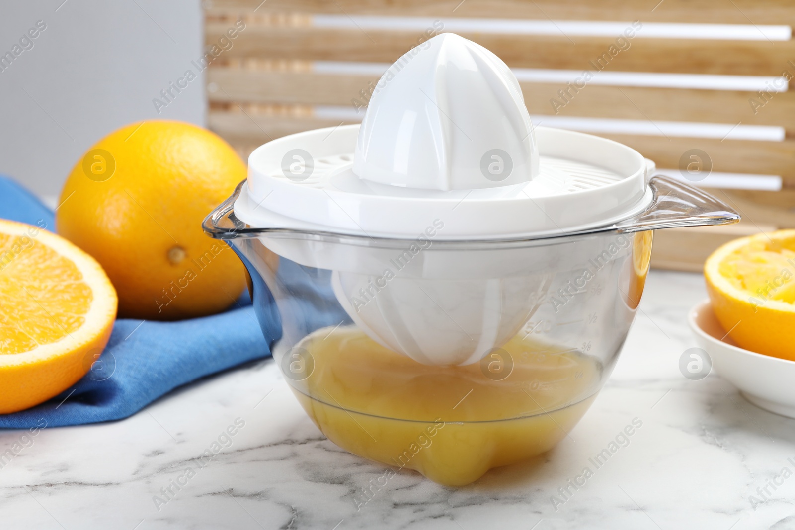 Photo of Plastic juicer and fresh oranges on white marble table, closeup