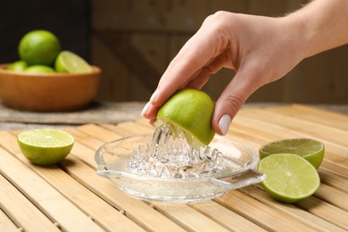 Photo of Woman squeezing juice of fresh lime with juicer at wooden table, closeup