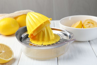 Photo of Plastic juicer and fresh lemons on white wooden table, closeup