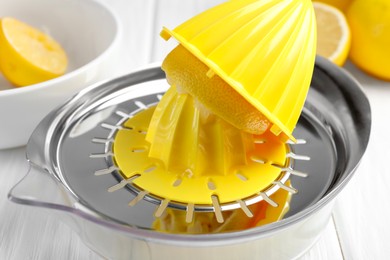 Photo of Plastic juicer and fresh lemons on white wooden table, closeup