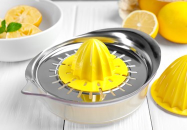 Photo of Plastic juicer and fresh lemons on white wooden table, closeup