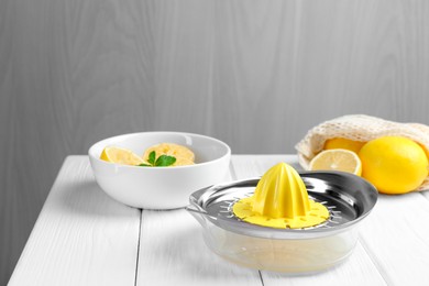 Photo of Plastic juicer and fresh lemons on white wooden table, closeup