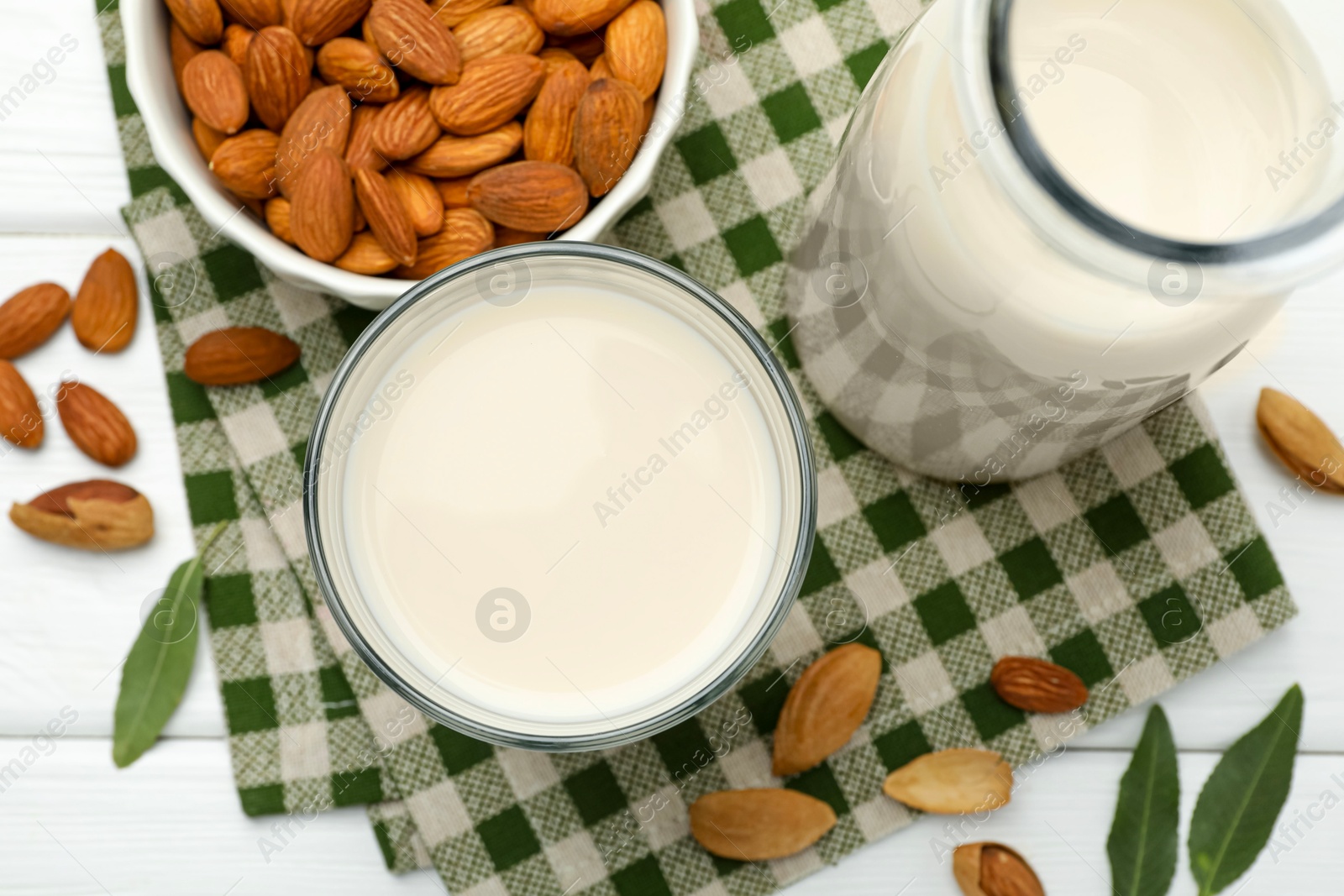 Photo of Fresh nut milk, almonds and green leaves on white wooden table, flat lay