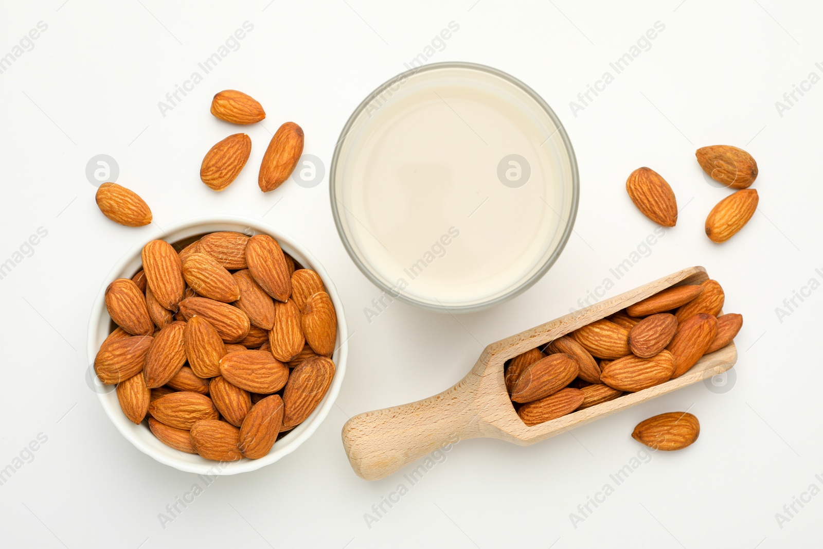 Photo of Fresh nut milk in glass and almonds on white table, flat lay