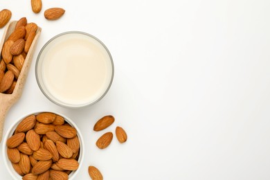 Photo of Fresh nut milk in glass and almonds on white table, flat lay. Space for text