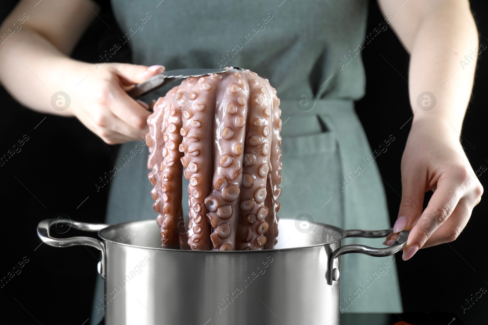 Photo of Woman taking boiled octopus from pan on stove, closeup