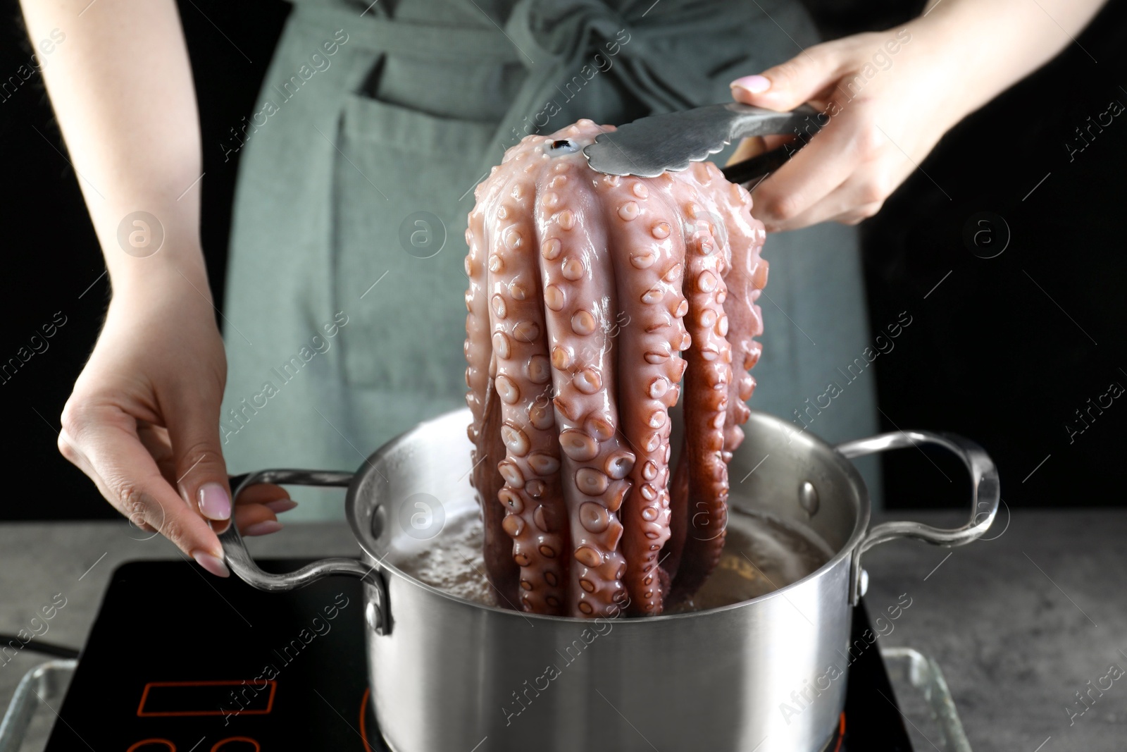 Photo of Woman taking boiled octopus from pan on stove, closeup