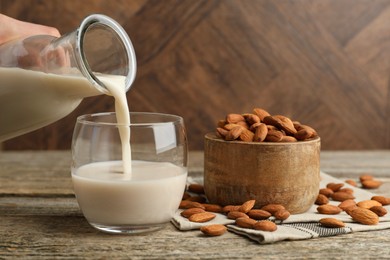 Woman pouring almond milk into glass and nuts at wooden table, closeup