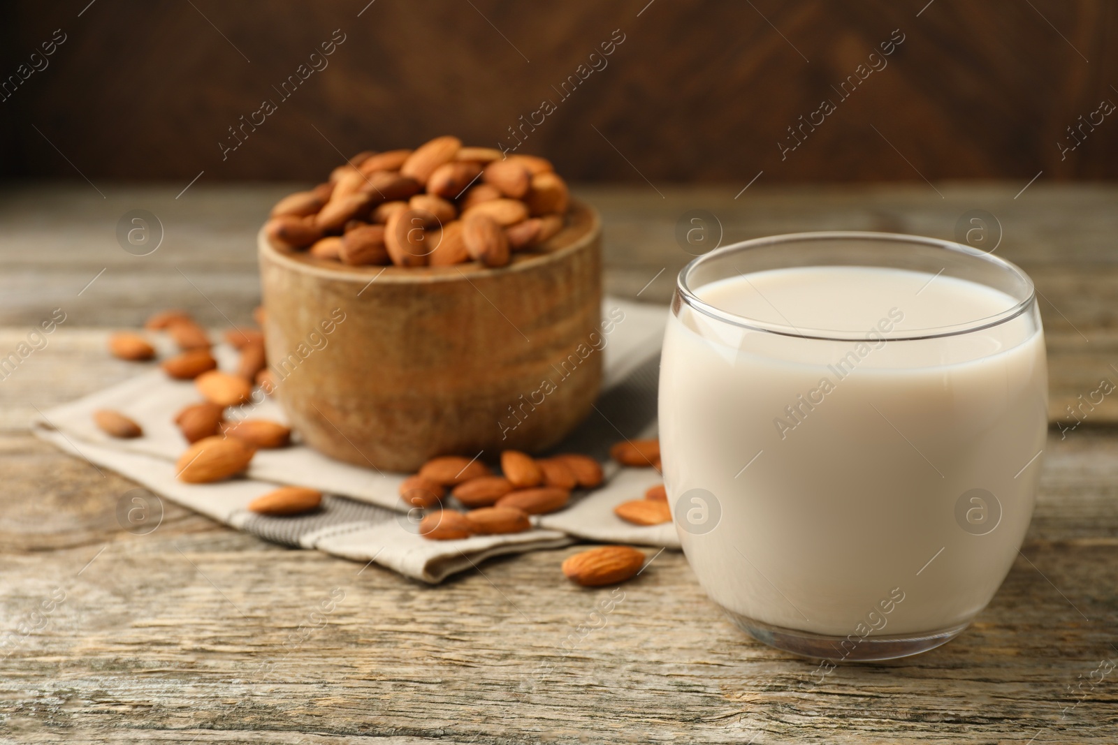 Photo of Fresh almond milk in glass and nuts on wooden table, closeup