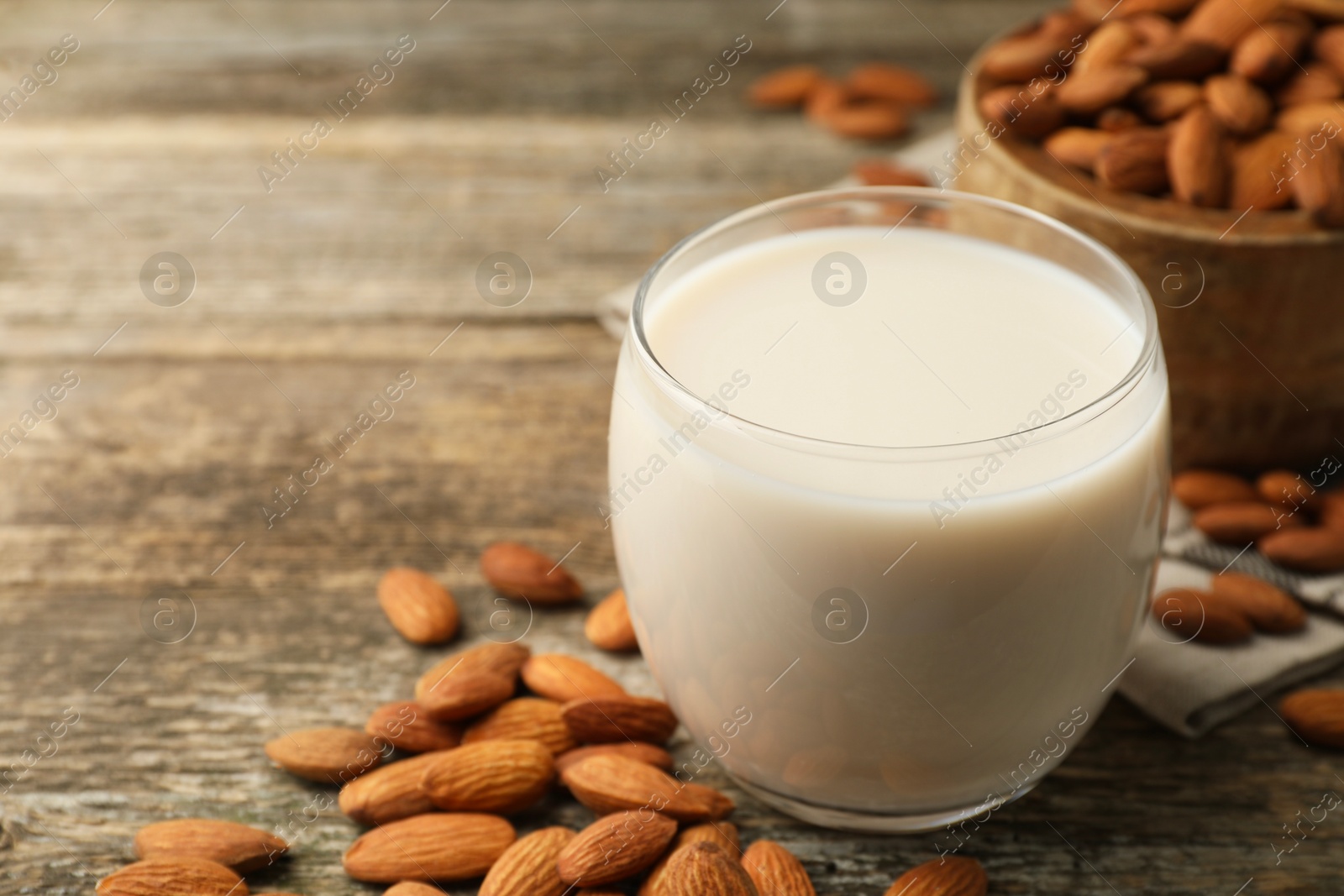 Photo of Fresh almond milk in glass and nuts on wooden table, closeup