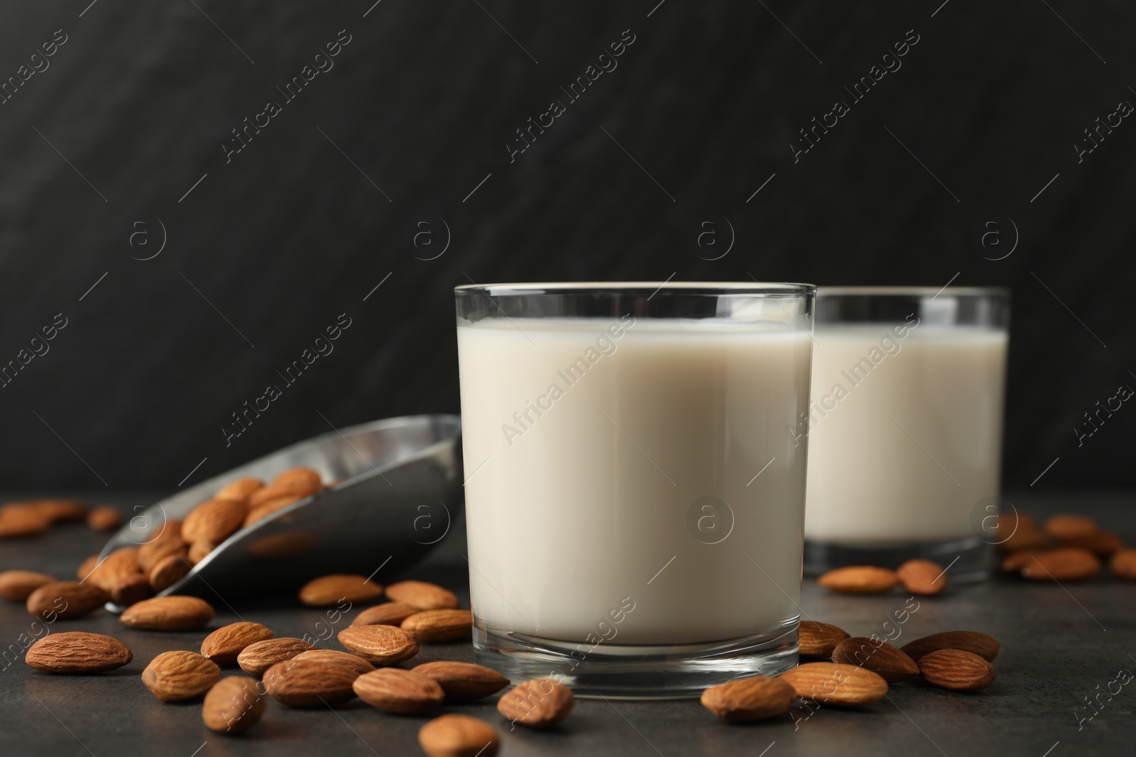 Photo of Fresh almond milk in glasses and nuts on dark grey table, closeup