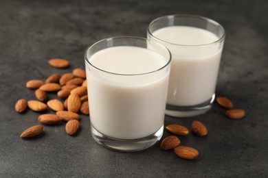 Photo of Fresh almond milk in glasses and nuts on dark grey table, closeup