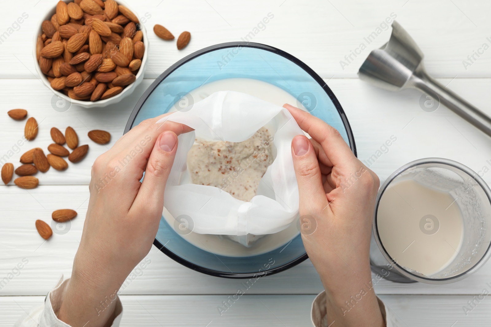 Photo of Woman making almond milk and nuts at white wooden table, top view