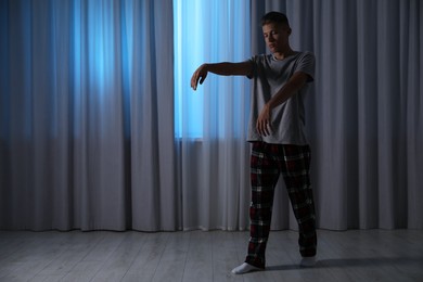 Photo of Young man suffering from sleepwalking at home, space for text