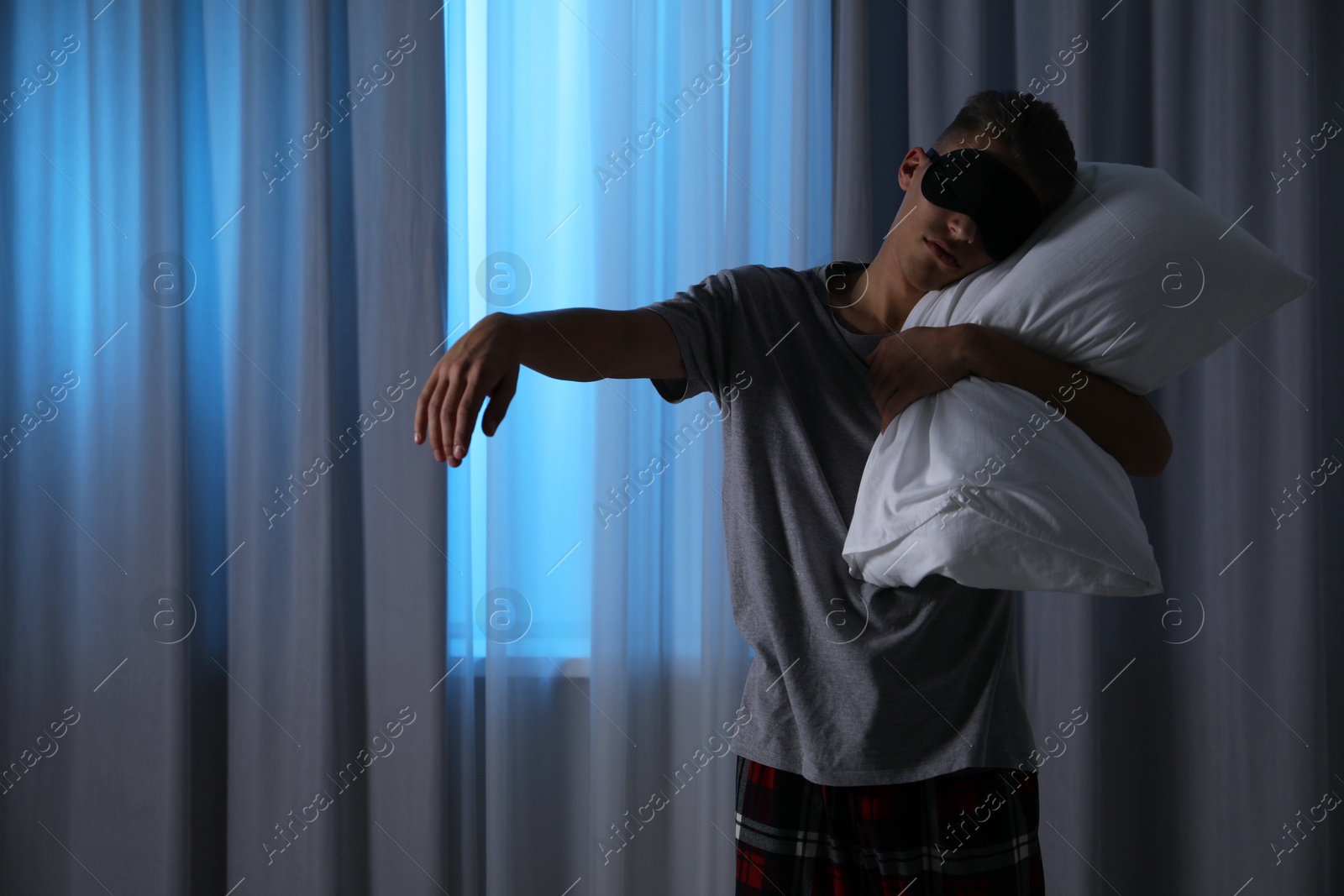 Photo of Young man suffering from sleepwalking at home, space for text