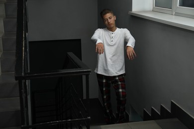 Photo of Young man suffering from sleepwalking on stairs indoors, space for text