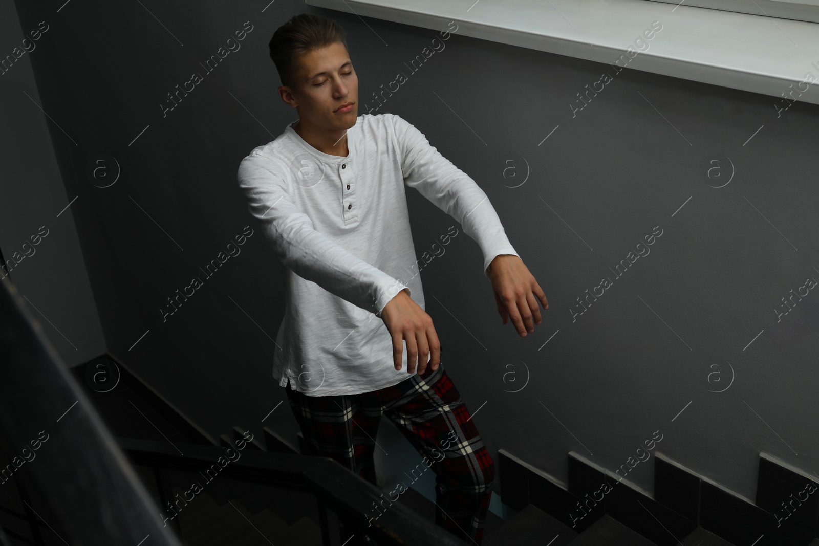 Photo of Young man suffering from sleepwalking on stairs indoors