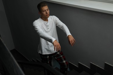 Young man suffering from sleepwalking on stairs indoors