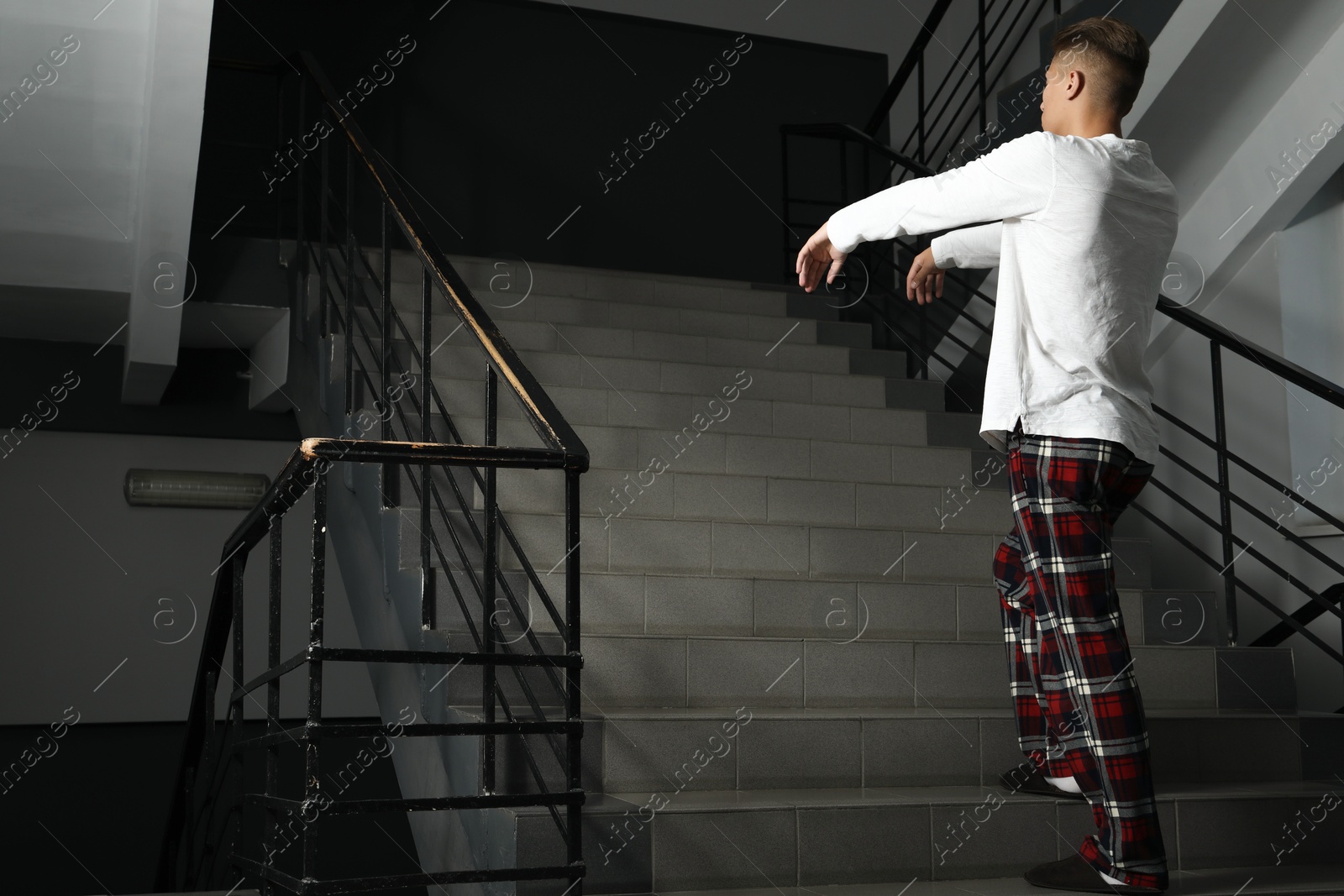 Photo of Young man suffering from sleepwalking on stairs indoors. Space for text