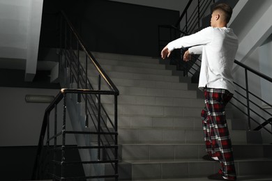 Photo of Young man suffering from sleepwalking on stairs indoors. Space for text