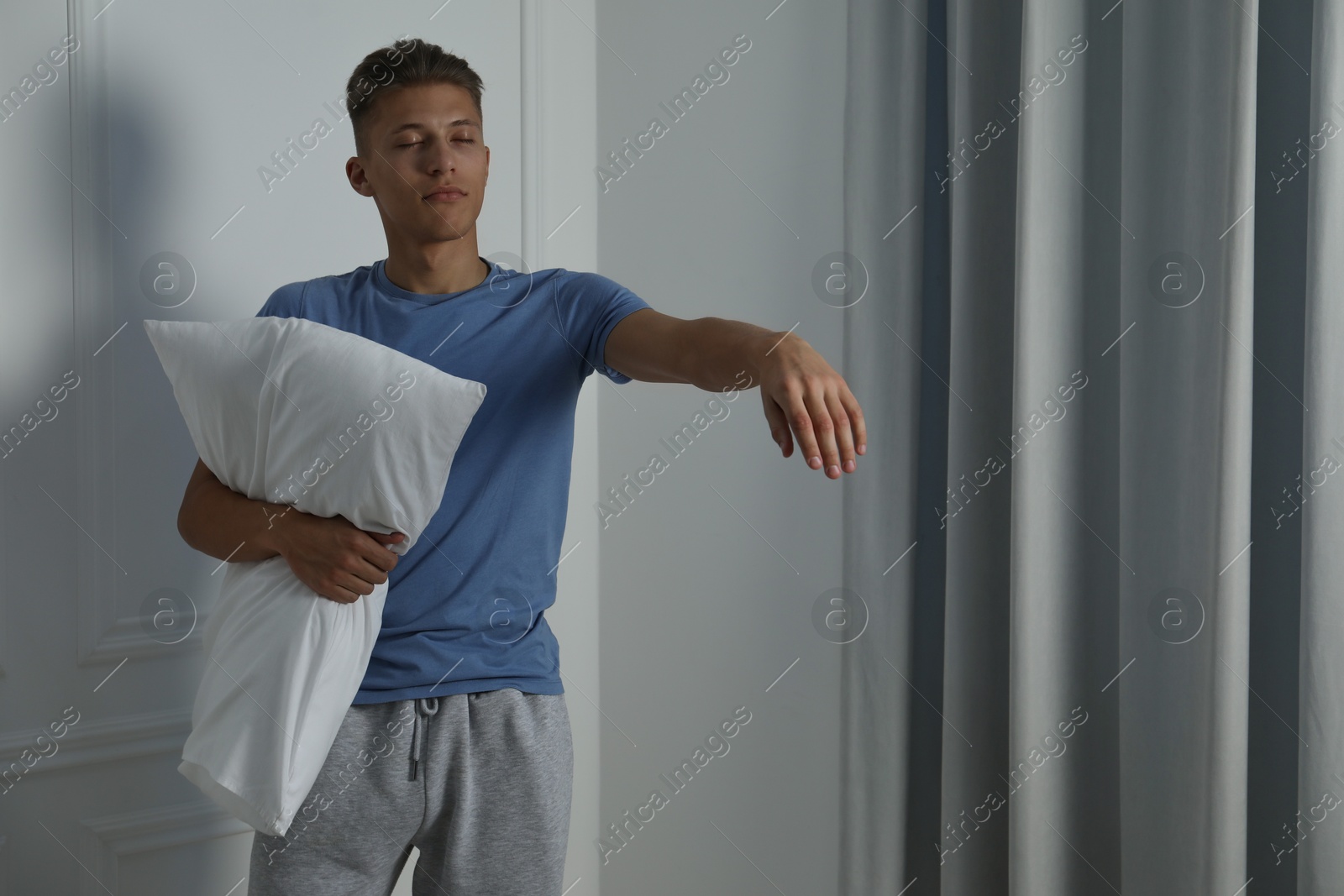 Photo of Young man with pillow suffering from sleepwalking at home, space for text