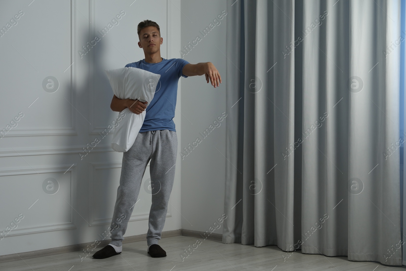 Photo of Young man with pillow suffering from sleepwalking at home, space for text