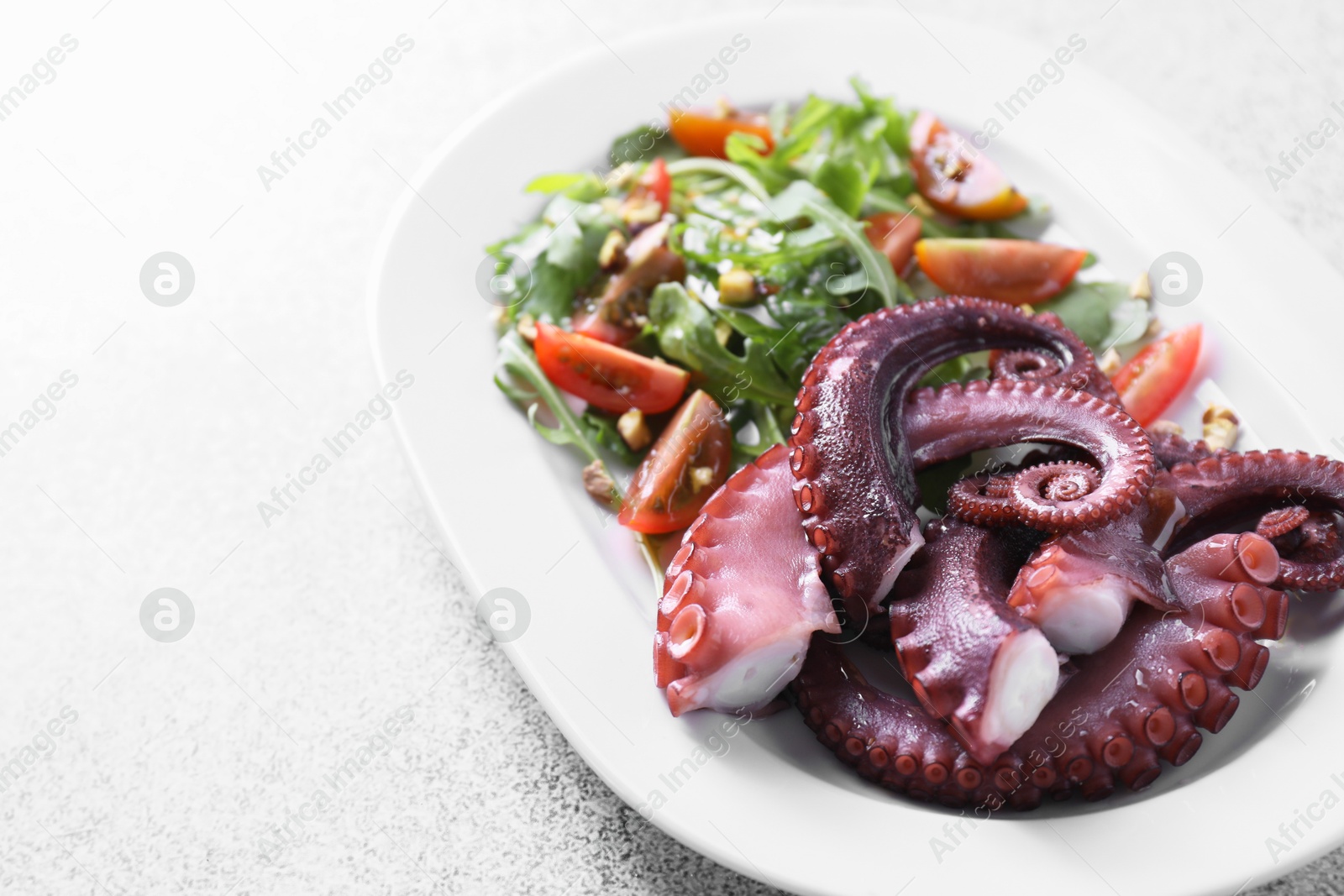 Photo of Plate with tasty boiled octopus tentacles and salad on grey textured table, closeup. Space for text