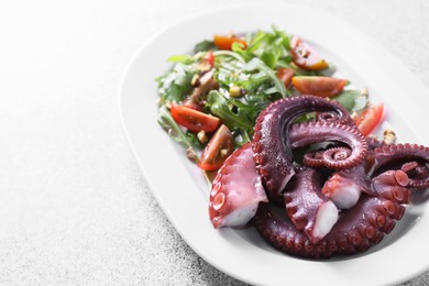 Photo of Plate with tasty boiled octopus tentacles and salad on grey textured table, closeup. Space for text