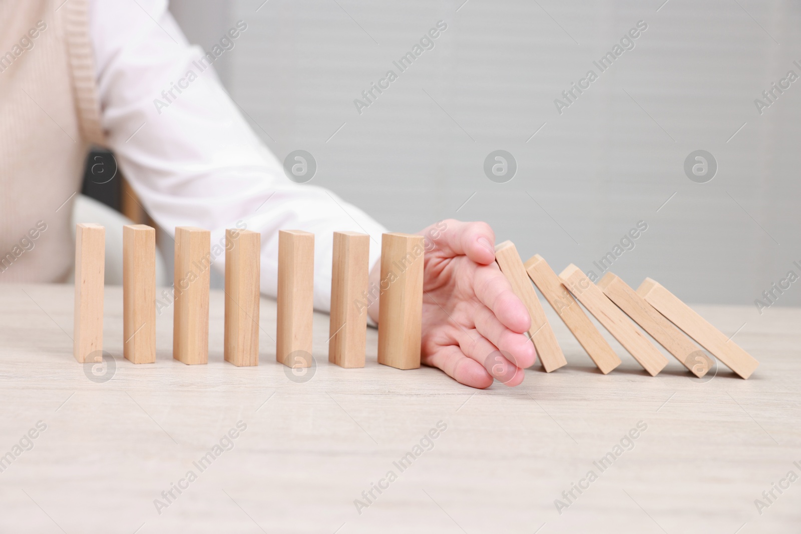 Photo of Woman stopping wooden blocks from falling at table, closeup. Domino effect