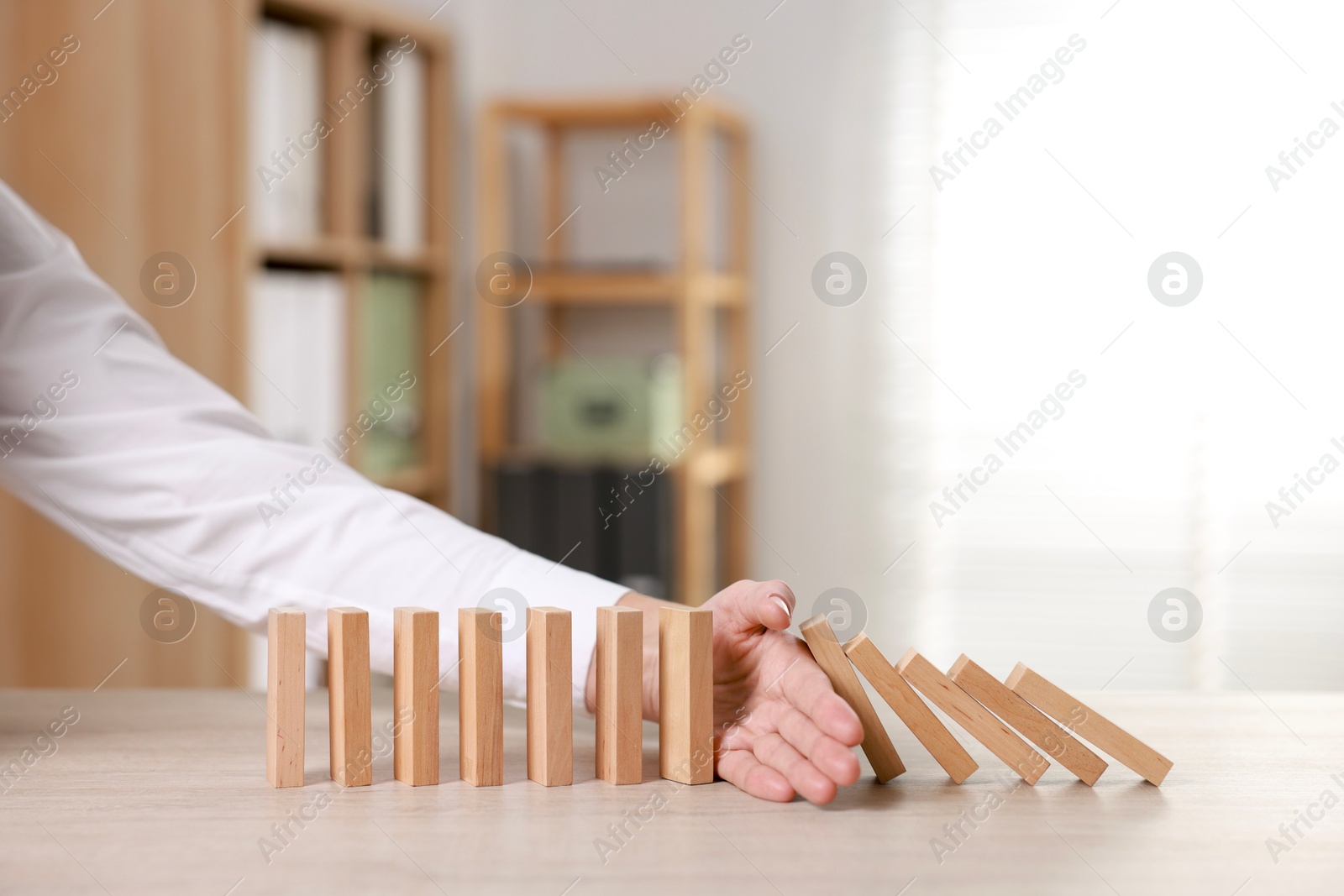 Photo of Woman stopping wooden blocks from falling at table, closeup. Domino effect