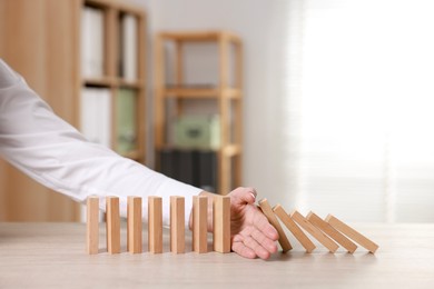 Photo of Woman stopping wooden blocks from falling at table, closeup. Domino effect