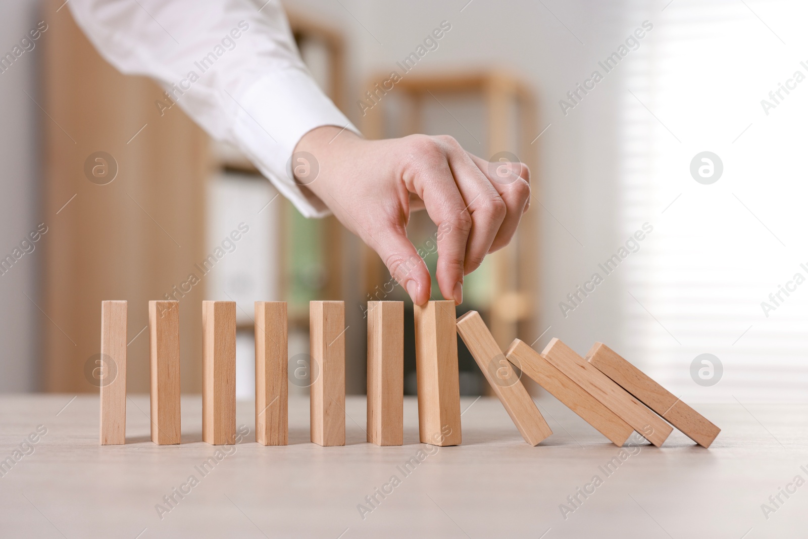 Photo of Woman stopping wooden blocks from falling at table, closeup. Domino effect