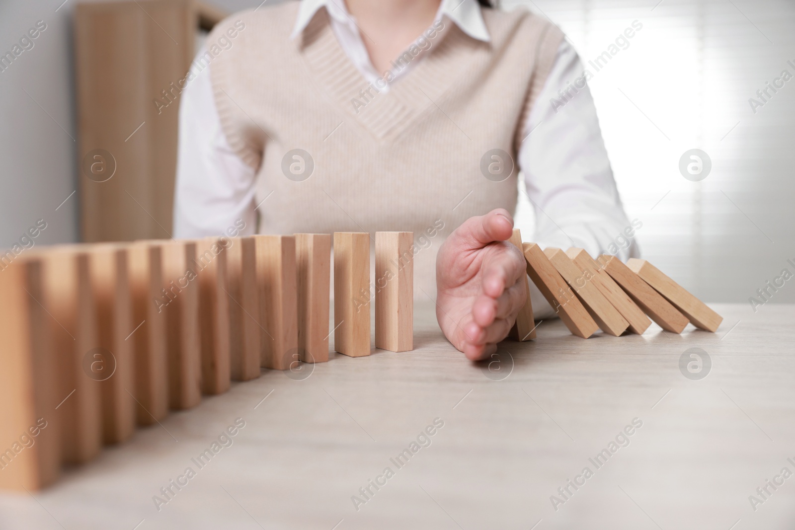 Photo of Woman stopping wooden blocks from falling at table, closeup. Domino effect