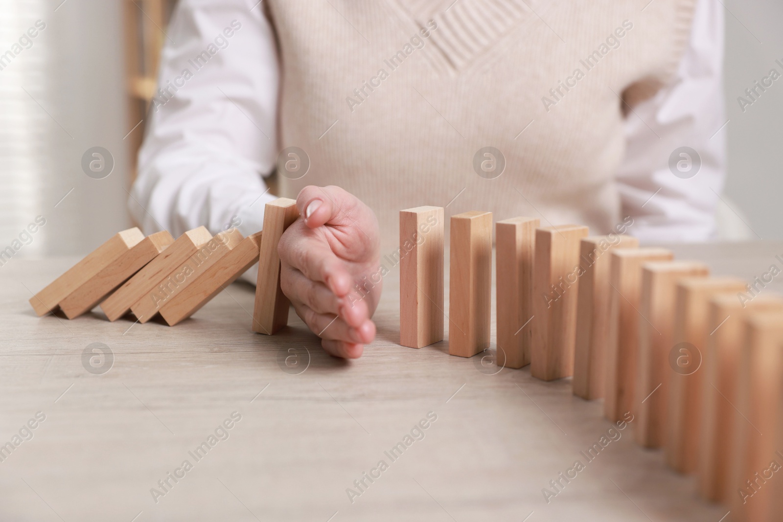 Photo of Woman stopping wooden blocks from falling at table, closeup. Domino effect