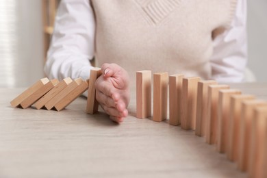 Photo of Woman stopping wooden blocks from falling at table, closeup. Domino effect