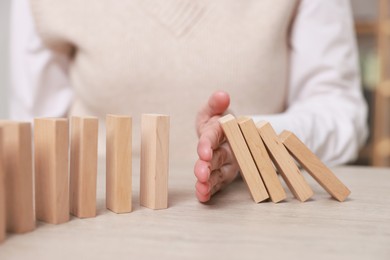 Photo of Woman stopping wooden blocks from falling at table, closeup. Domino effect