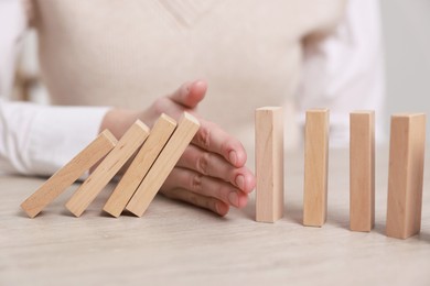 Photo of Woman stopping wooden blocks from falling at table, closeup. Domino effect