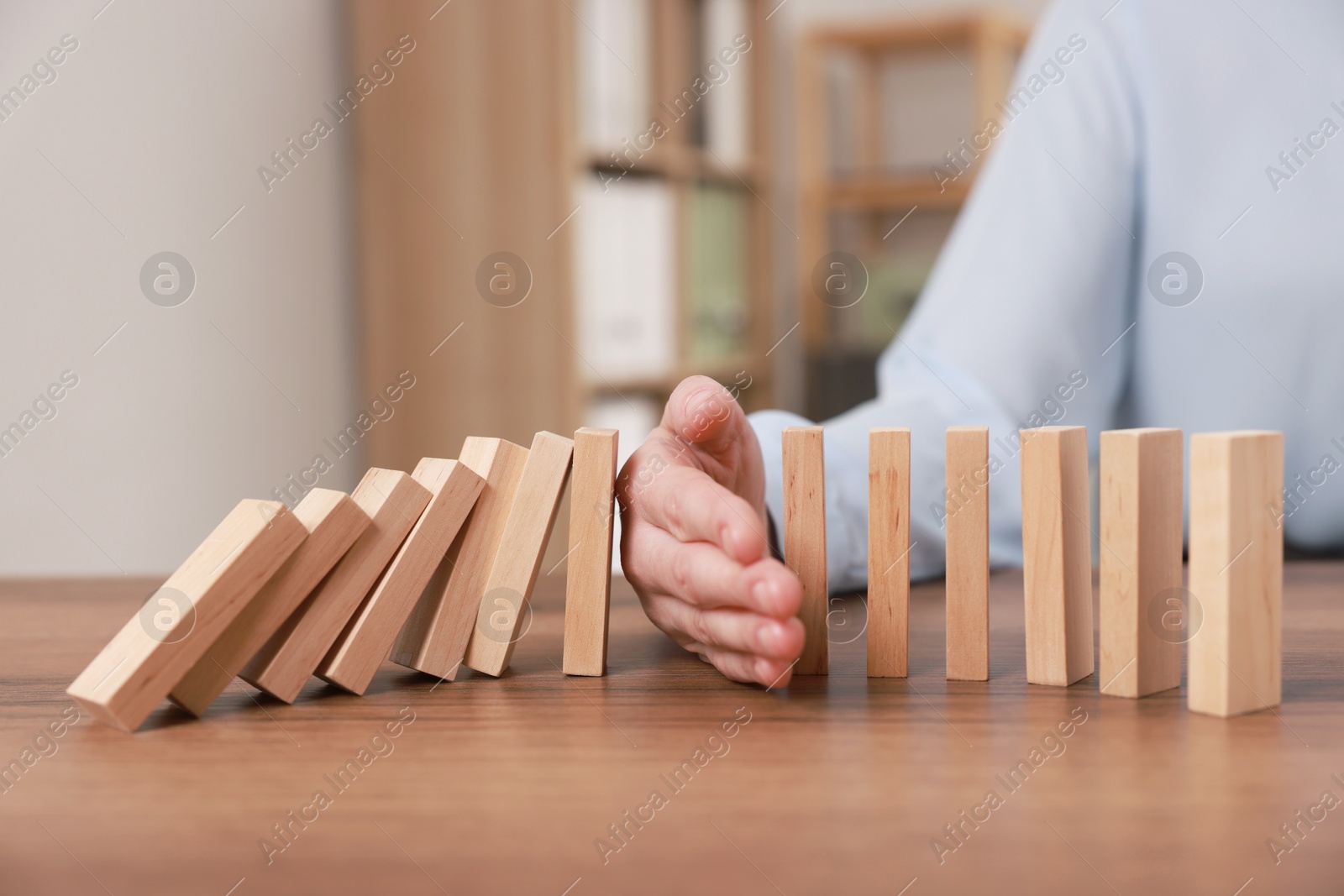 Photo of Woman stopping wooden blocks from falling at table, closeup. Domino effect