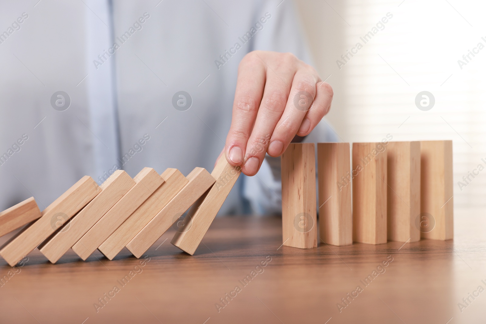 Photo of Woman stopping wooden blocks from falling at table, closeup. Domino effect