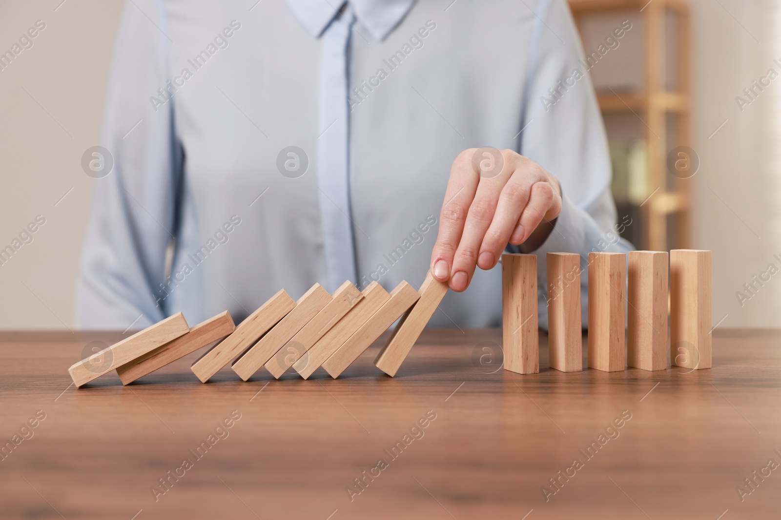 Photo of Woman stopping wooden blocks from falling at table, closeup. Domino effect