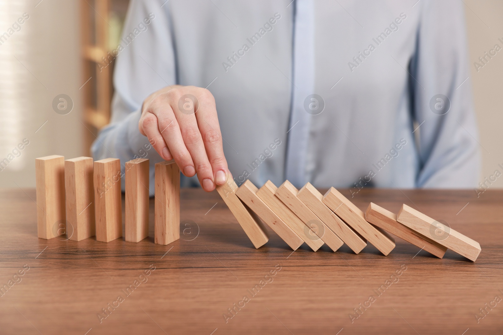 Photo of Woman stopping wooden blocks from falling at table, closeup. Domino effect