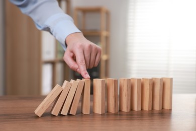 Photo of Woman stopping wooden blocks from falling at table, closeup. Domino effect