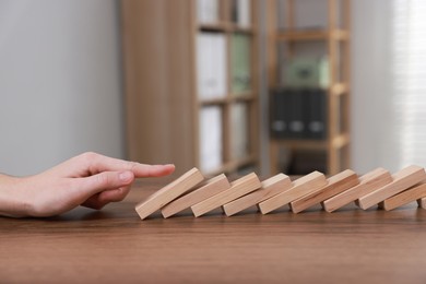 Photo of Domino effect. Woman pushing wooden blocks at table, closeup