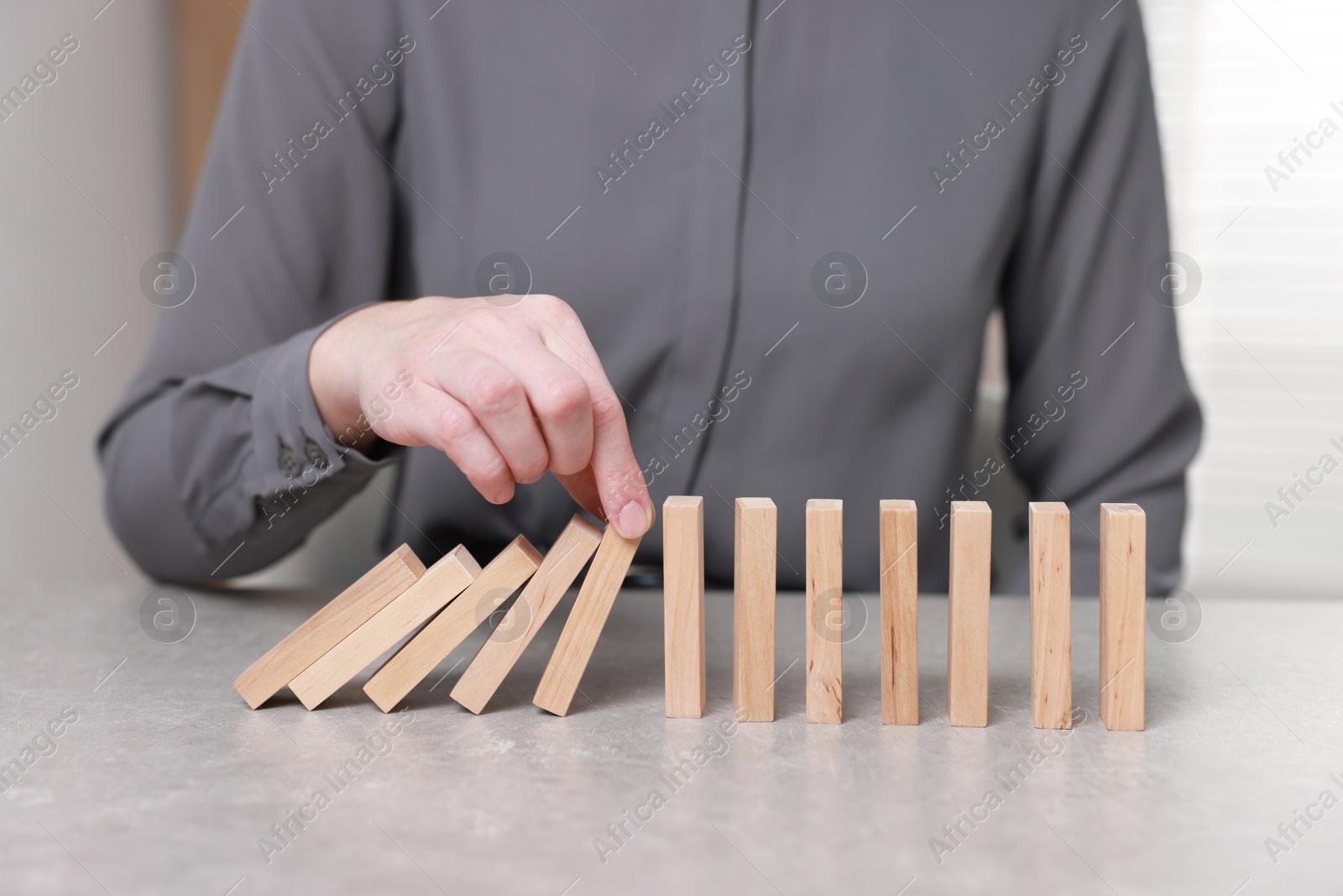 Photo of Woman stopping wooden blocks from falling at table, closeup. Domino effect