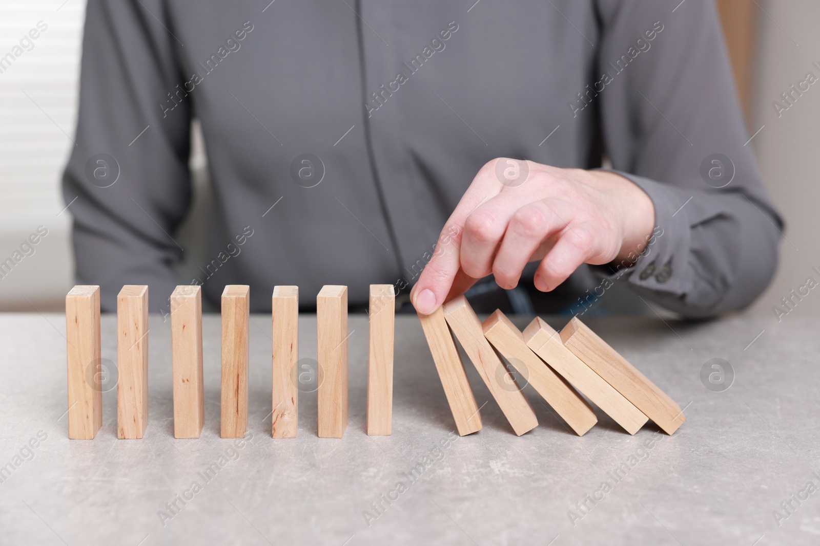 Photo of Woman stopping wooden blocks from falling at table, closeup. Domino effect