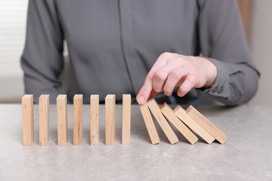 Photo of Woman stopping wooden blocks from falling at table, closeup. Domino effect