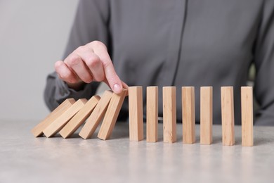 Photo of Woman stopping wooden blocks from falling at table, closeup. Domino effect